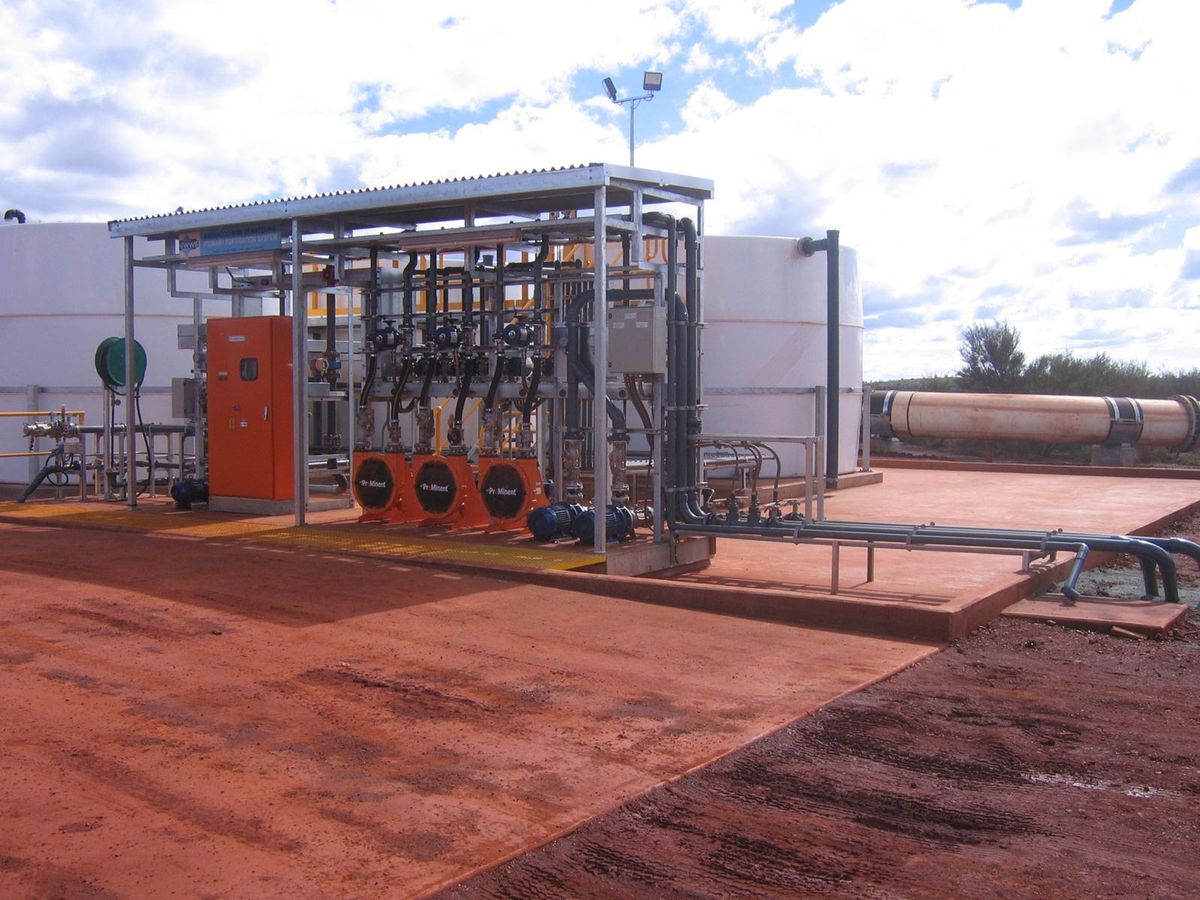 Valves, pipework and pumps under a roofed frame between two site tanks, with pipework running out across the pad.